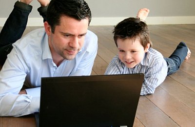 Vater und Sohn lernen gemeinsam am Laptop Vater und Sohn liegen auf dem Boden und schauen gemeinsam auf einen Laptop