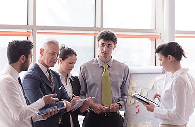 Team bespricht Geschäftsstrategie im Büro Fünf Geschäftsleute stehen zusammen und diskutieren Unterlagen in modernem Büro